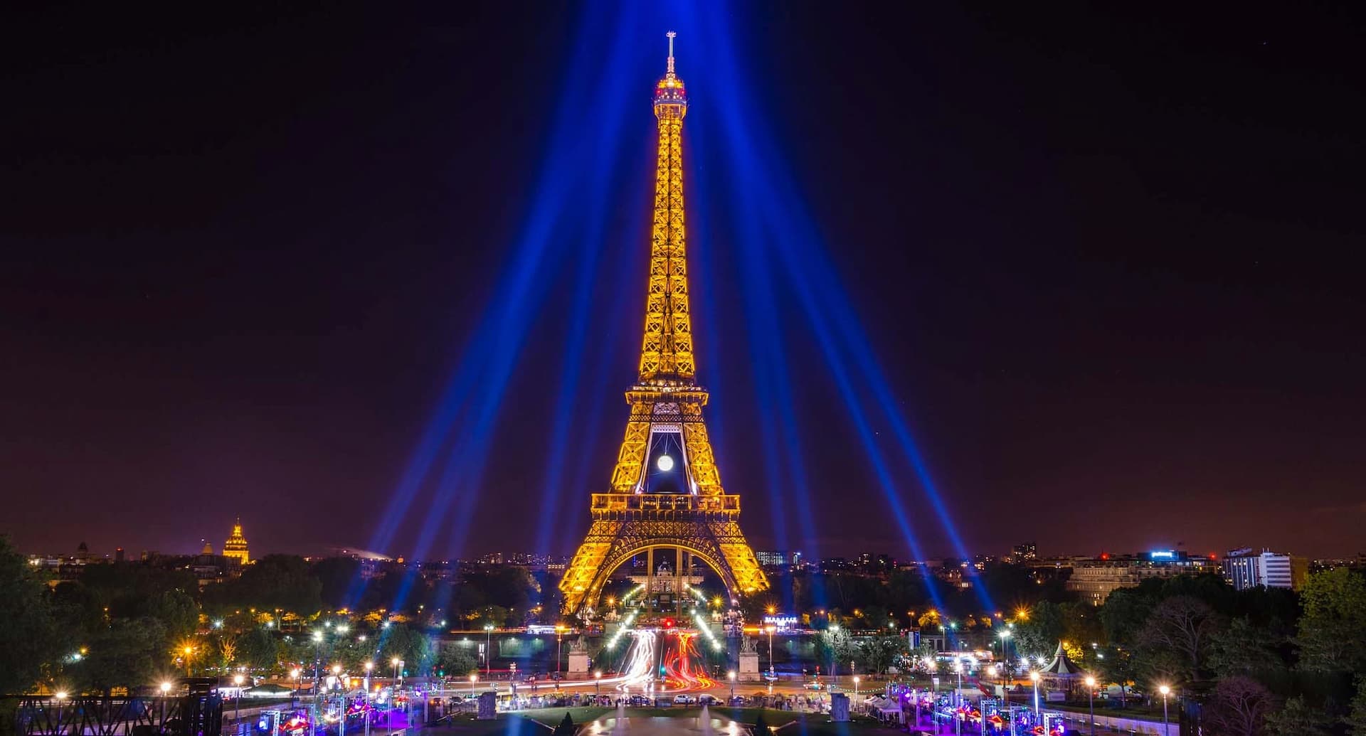 A nighttime view of the illuminated Eiffel Tower with blue light beams shining from its top
